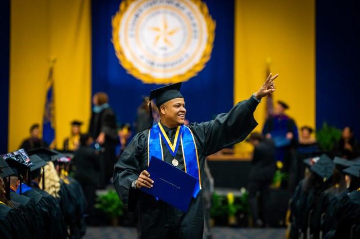 A&M-Commerce graduate extends arm and shows peace sign after receiving diploma.